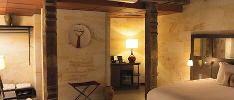 Een gezellige slaapkamer met een groot bed, een bureau met stoel, een klein tafeltje met lamp en een decoratieve vaas.