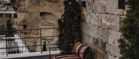 Un edificio de piedra con una gran formación rocosa, asientos exteriores con cojines a rayas y una planta en maceta.