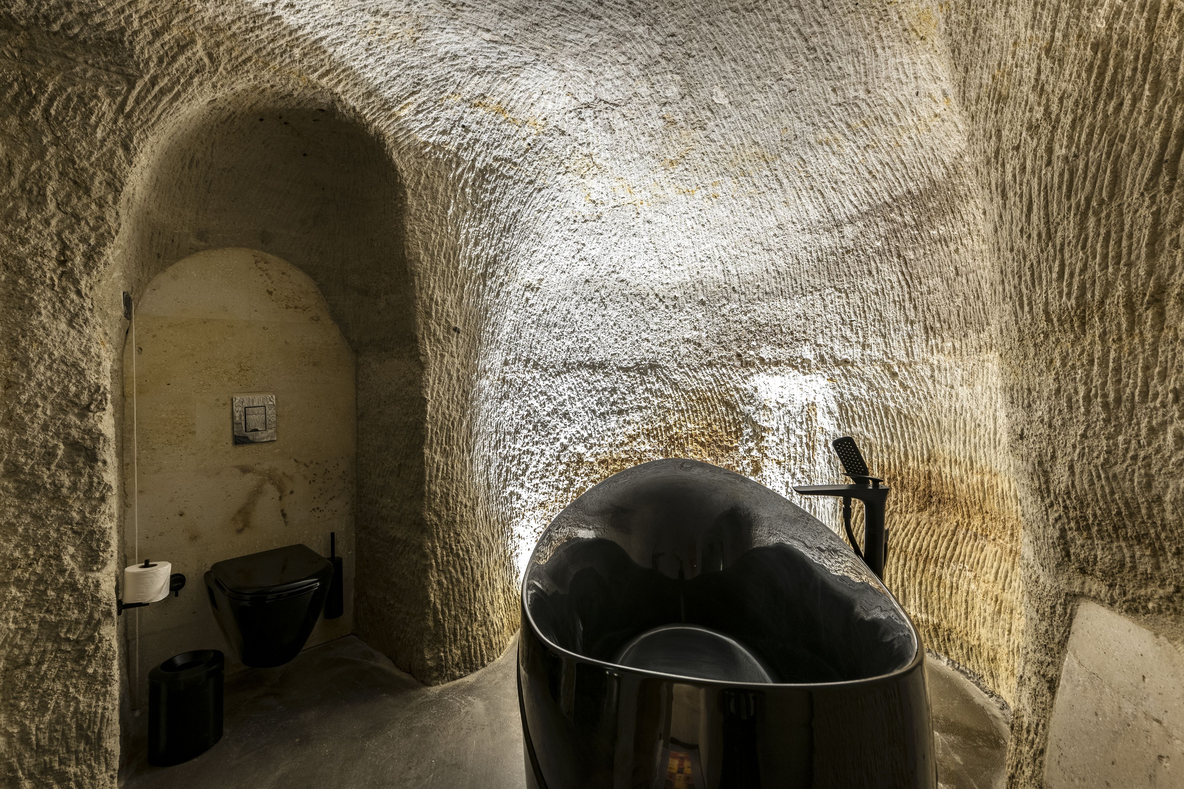 A stone-walled room with a large, round, black object in the center, a small sink, and a toilet.