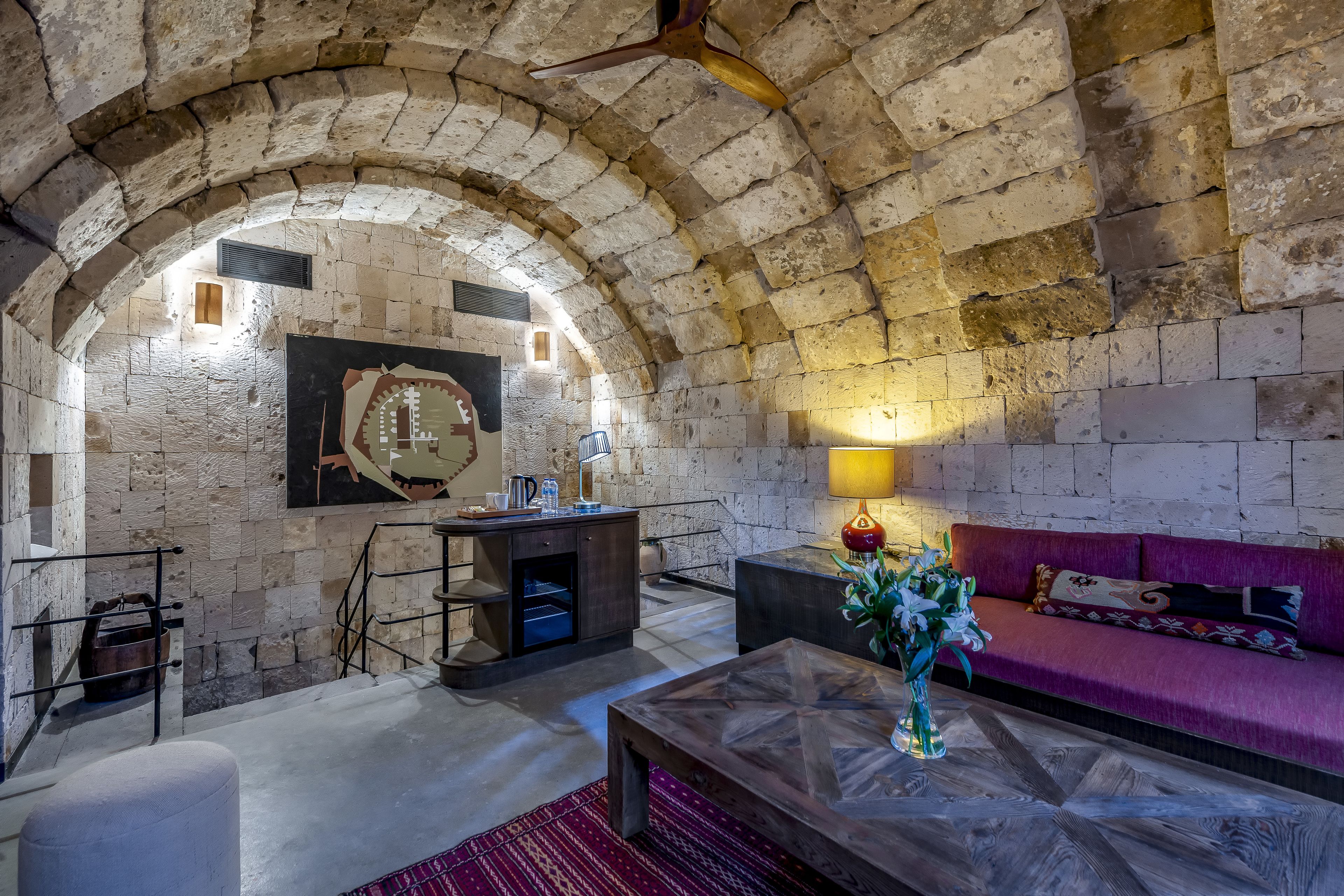 A cozy room with stone walls, a wooden bench, a sofa, and a table with a vase.