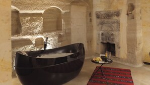 Una habitación de paredes de piedra con una bañera negra, una chimenea y una alfombra estampada.