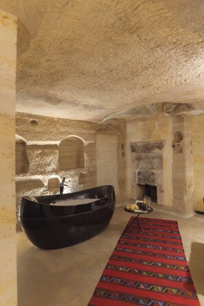 Una habitación de paredes de piedra con una bañera negra, una chimenea y una alfombra estampada.