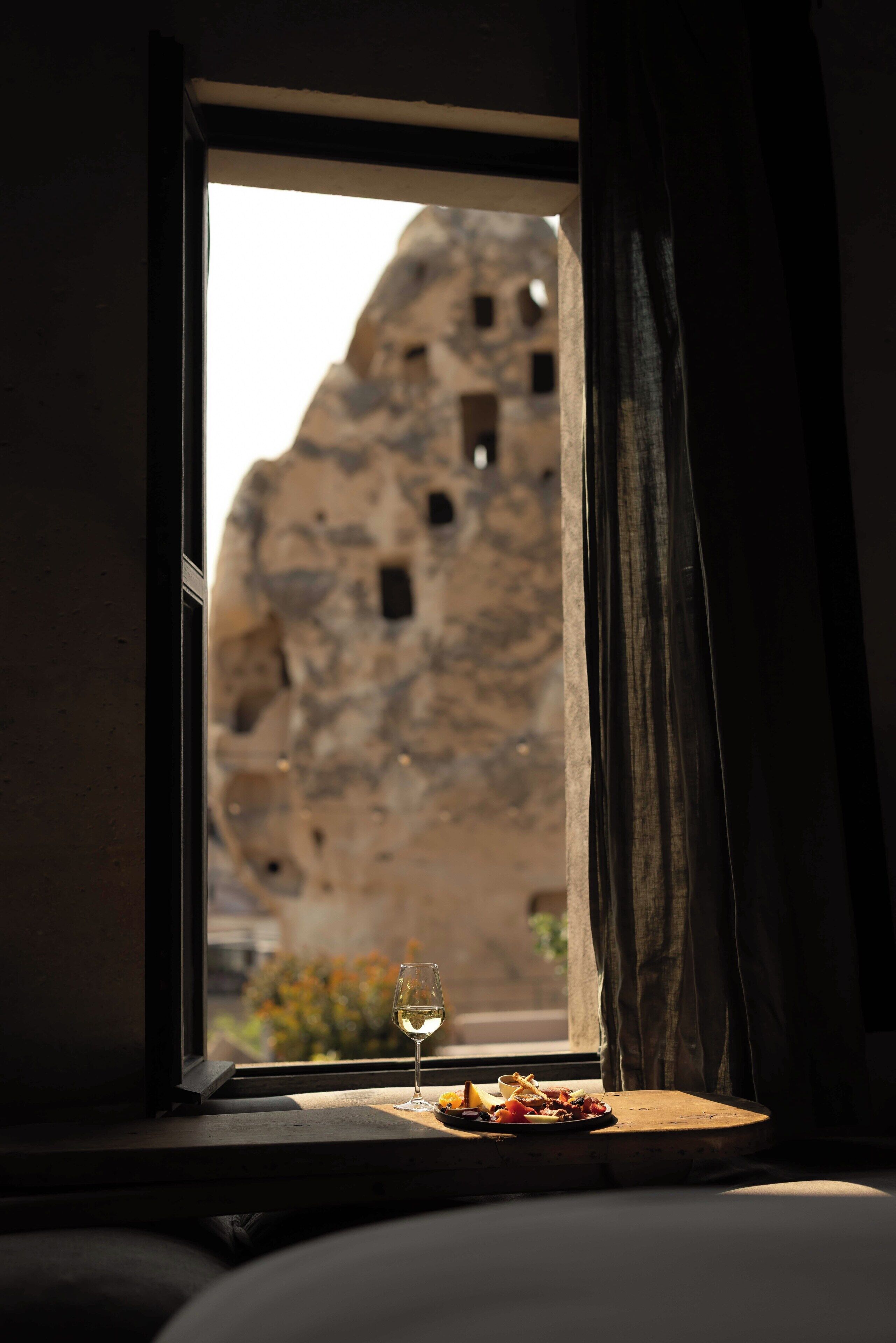 A window with a view of a rock formation and a table with a glass of wine and food.
