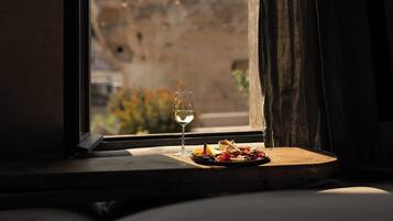 A window with a view of a rock formation and a table with a glass of wine and food.