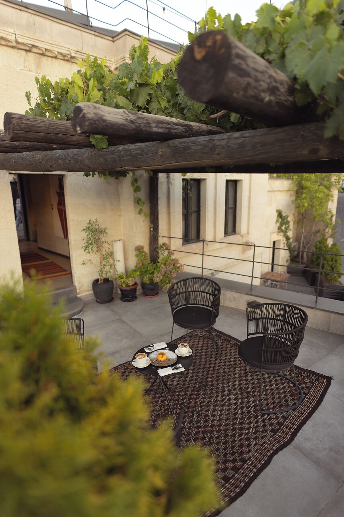 Eine Dachterrasse mit einem runden Tisch, zwei schwarzen Stühlen und Topfpflanzen.