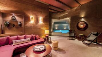 Un'area spa moderna con una parete in legno, una zona relax con un divano rosa, un tavolino rotondo e una poltrona.