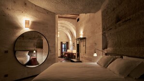A bedroom with a large bed, a round mirror, and a view of a dining area through an arched doorway. - Carus Cappadocia (Nevsehir)