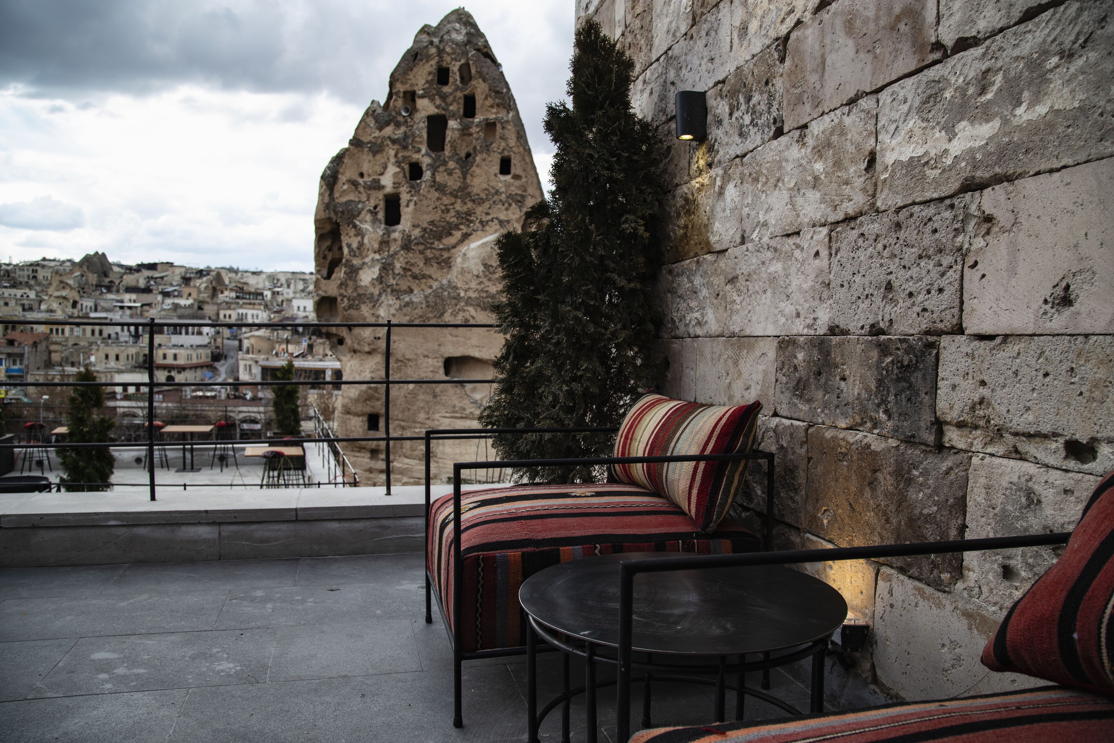A rooftop terrace with a stone wall, a small Christmas tree, and a seating area with a striped cushion.