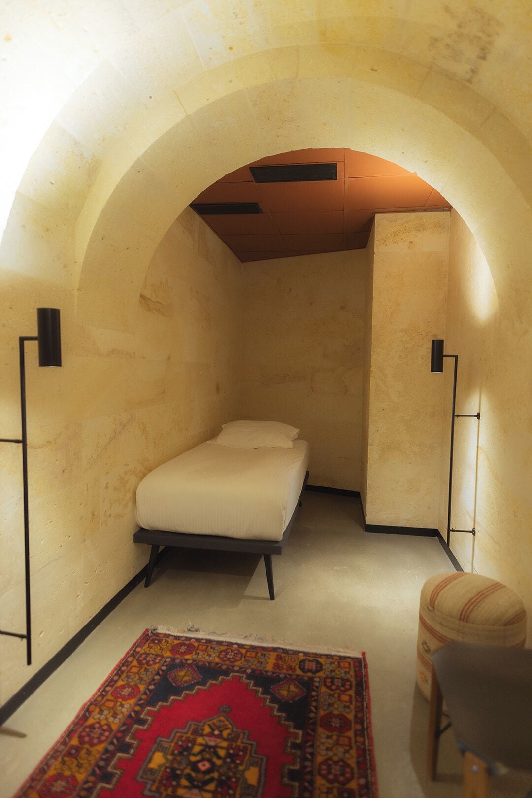 Una habitación pequeña y acogedora con una cama individual, un tapete estampado y una silla.