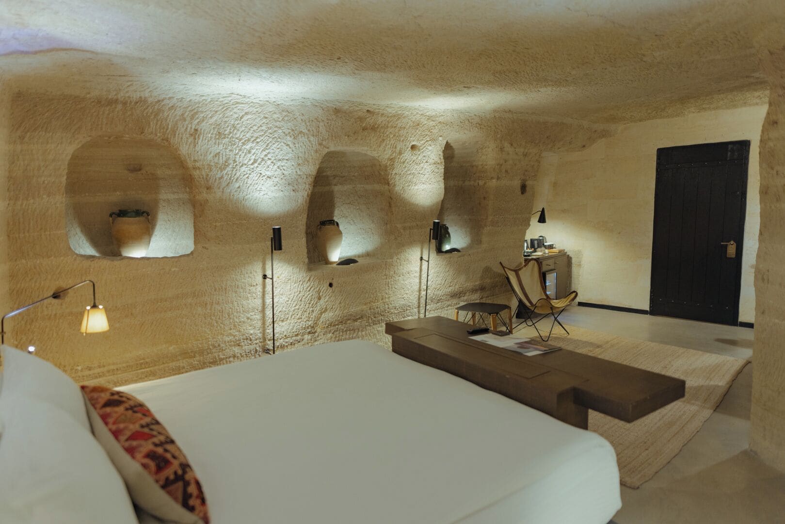 Un dormitorio con cama, escritorio, silla, lámpara y puerta.