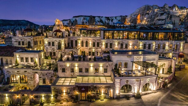 A multi-story hotel with a central courtyard, stone facades, and a mountain backdrop. - Carus Cappadocia (Nevsehir)