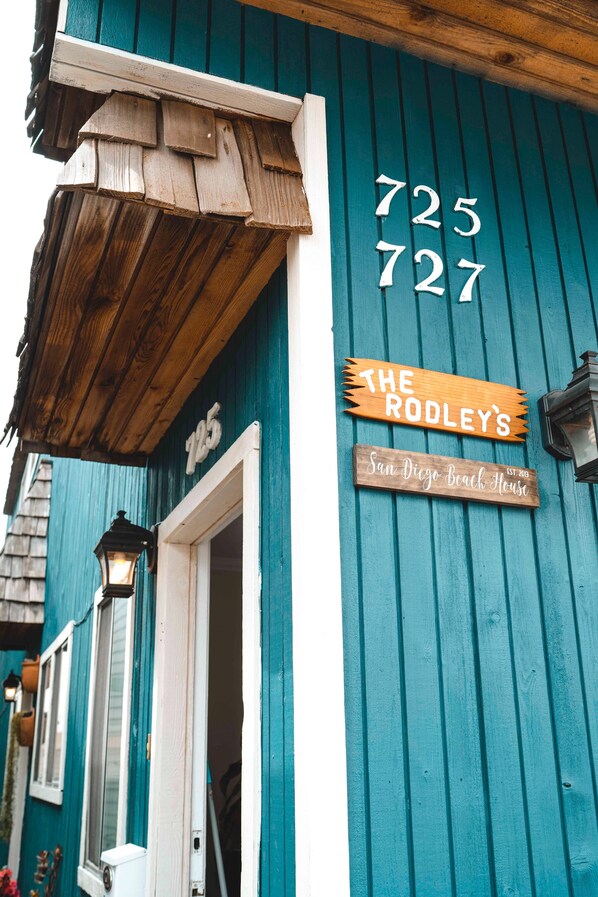 A teal building with a wooden sign reading "The Rodley's San Diego Beach House."