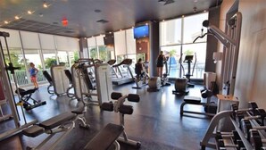 A gym with various exercise equipment, large windows, and a TV screen. - 2 Bedroom Unit Across From Ocean @ Beachwalk Resort (Hallandale Beach)