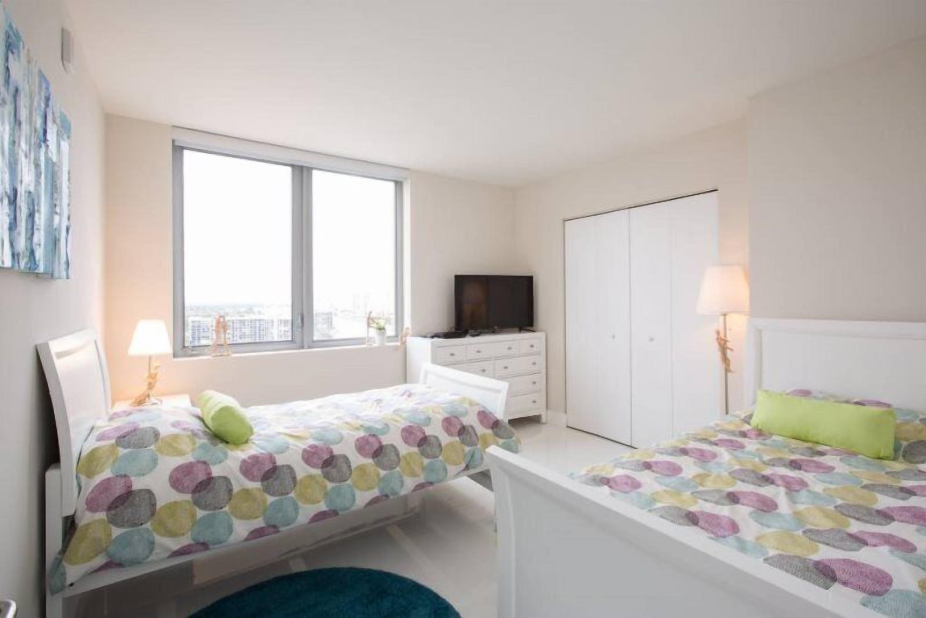 Quarto com duas camas, cômoda, televisão e guarda-roupa.