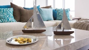 A modern living room with a glass coffee table, a sofa with patterned cushions, and two model sailboats. - Ocean View 3 Bed 3 Bath Across The Beach @ Beachwalk (Hallandale Beach)