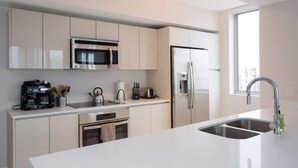 A modern kitchen with white cabinetry, stainless steel appliances, and a large island with a sink. - Ocean View 3 Bed 3 Bath Across The Beach @ Beachwalk (Hallandale Beach)