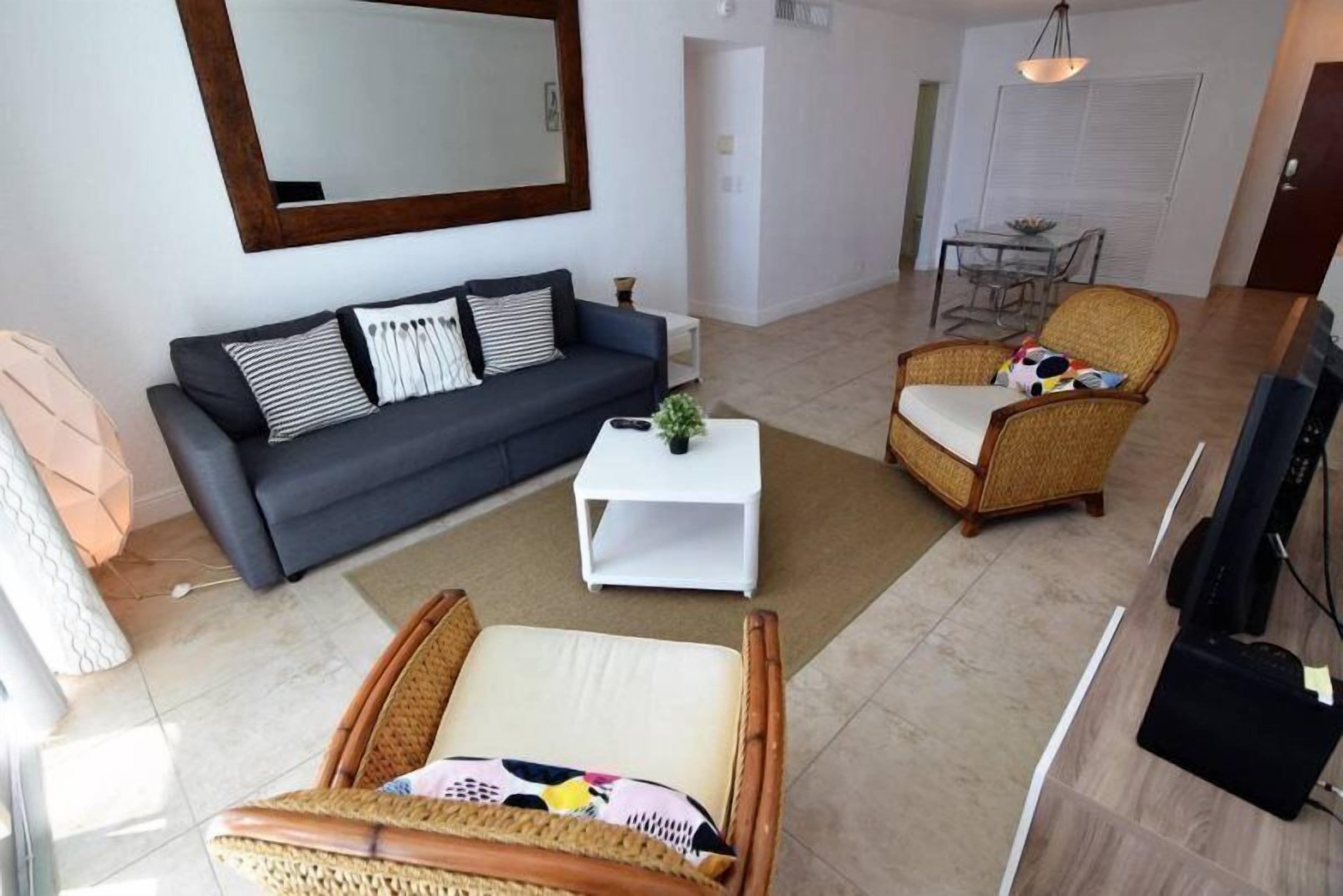 En moderne stue med en grå sofa, et hvidt sofabord, fletstole og et stort spejl på væggen.