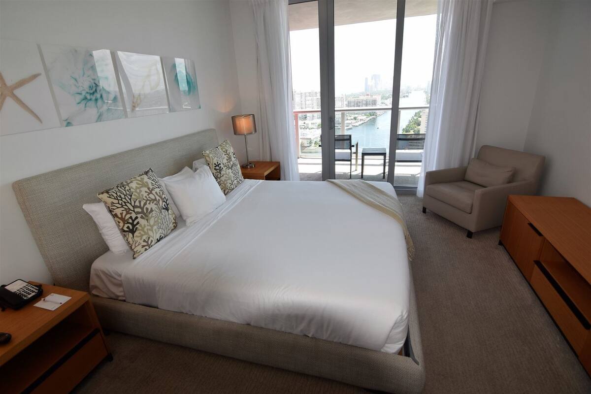 Une chambre d’hôtel avec un grand lit, un bureau, une chaise et une vue sur la ville par la fenêtre.