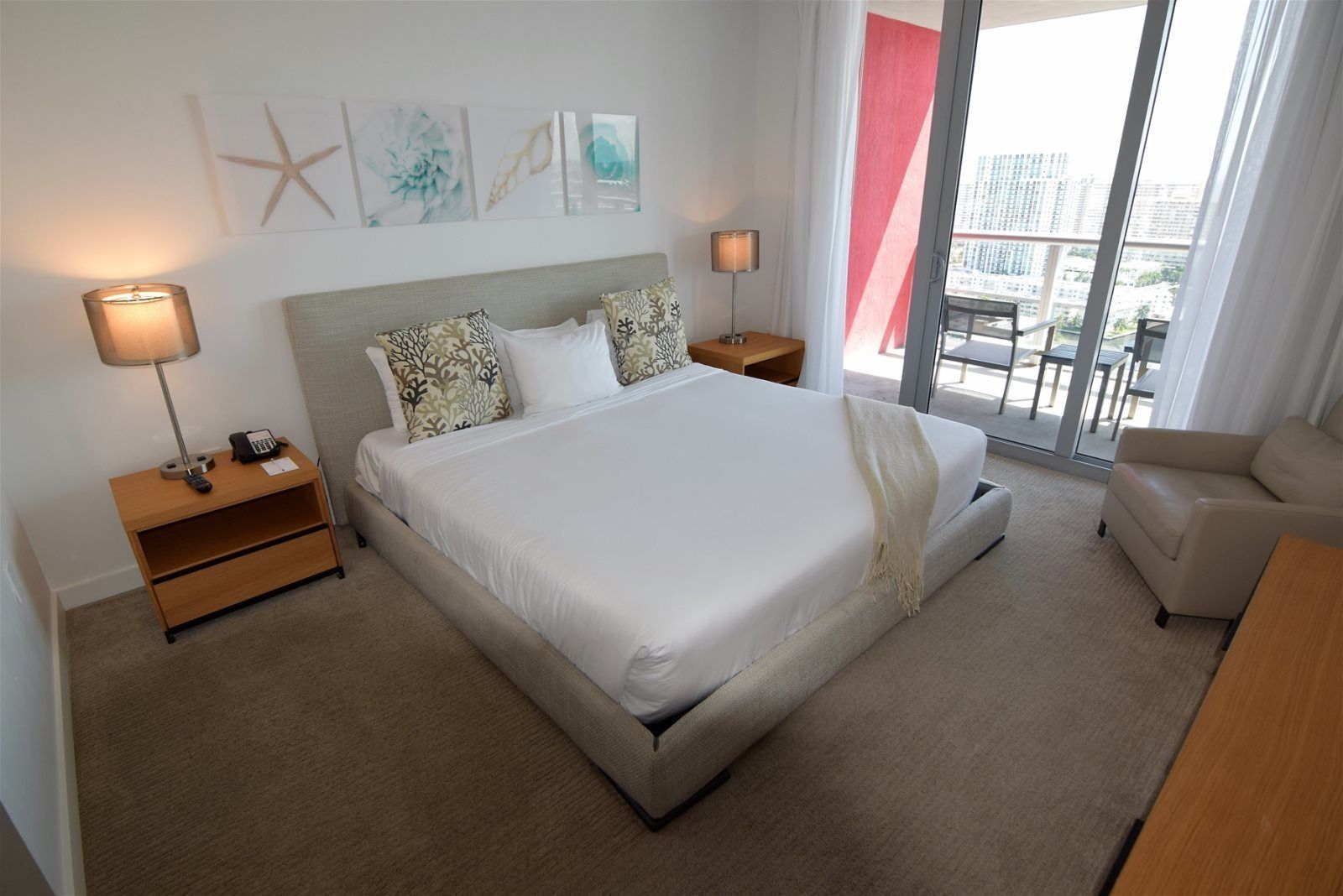 Una camera d'albergo moderna con un letto grande, due comodini, una sedia e un balcone con vista sulla città.