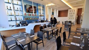A restaurant with a bar area, wooden flooring, and black chairs.