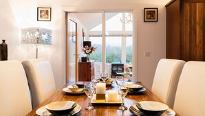 Comedor con mesa de madera dispuesta para cuatro, una araña y vista a un patio exterior a través de puertas de cristal.