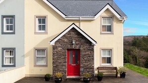 Una casa de dos pisos con puerta roja, fachada de piedra y camino de entrada pavimentado.