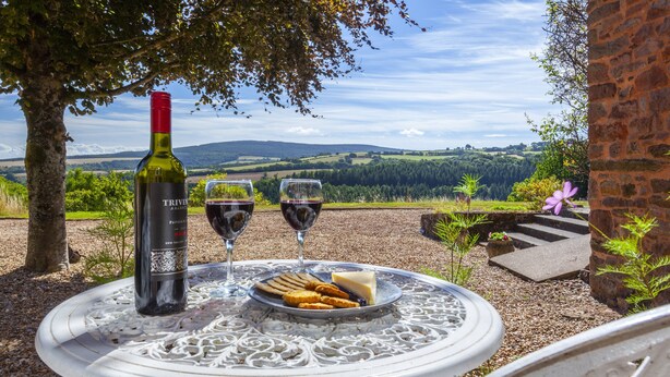 A table with a bottle of wine, two glasses, and a plate of cheese and crackers. - East Harwood Farm Cottage, Timberscombe (Minehead)