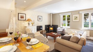 A living room with a fireplace, sofa, dining table, and chairs. - East Harwood Farm Cottage, Timberscombe (Minehead)
