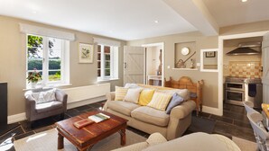 A living room with a sofa, armchair, coffee table, and a view of the garden through a window. - East Harwood Farm Cottage, Timberscombe (Minehead)