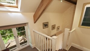 A staircase with a wooden handrail, a white door, and a window with a view of greenery. - East Harwood Farm Cottage, Timberscombe (Minehead)