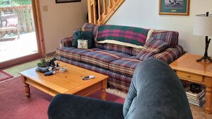 Un salon chaleureux avec un escalier en bois, un canapé à carreaux, une table basse et une lampe.
