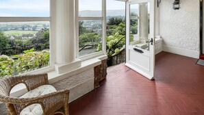 A room with large windows, a wicker chair, a fireplace, and a view of the countryside. - Redway Lodge, Porlock (Porlock)