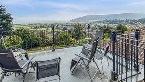 A balcony with two chairs and a table, overlooking a scenic landscape with fields and distant hills. - Redway Lodge, Porlock (Porlock)