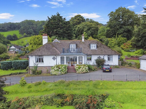 Ein zweistöckiges Haus mit Veranda, Auffahrt und umzäunter Garten.