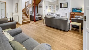 A spacious living room with a wooden staircase, grey sofas, and a fireplace. - Redway Lodge, Porlock (Porlock)