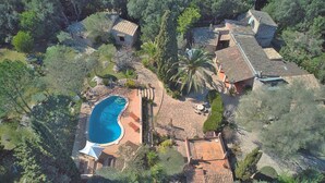 An aerial view of a property with a swimming pool, stone pathways, and multiple buildings surrounded by dense vegetation.