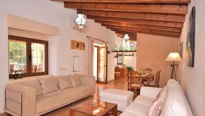 A living room with a beige sofa, a white sofa, a wooden coffee table, and a dining area with wooden chairs and a table.
