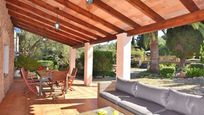 A covered patio with a wicker sofa, a dining table with chairs, and a glass coffee table.