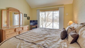 Une chambre à coucher avec un grand lit, une commode en bois, une télévision et une fenêtre donnant sur des arbres.