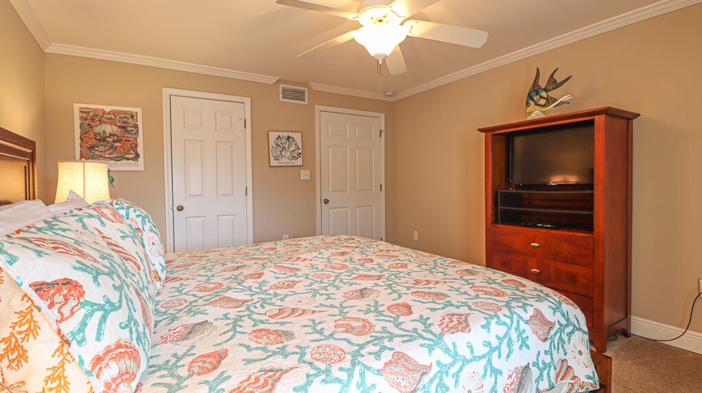 A bedroom with a bed, two doors, a ceiling fan, and a wooden cabinet.