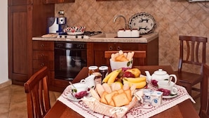 A kitchen with wooden cabinets, a microwave, a toaster, and a sink. There is a table with a basket of bread, bananas, and a teapot.