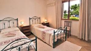 A bedroom with two single beds, a nightstand, a chair, and a window with curtains.