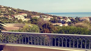A terrace with a table and chairs, overlooking a coastal town with buildings and a clear sky. - Le Marina (L'île-Rousse)