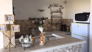 A kitchen with a microwave, a refrigerator, a bread basket, and a shelf with kitchen utensils. - Le Marina (L'île-Rousse)