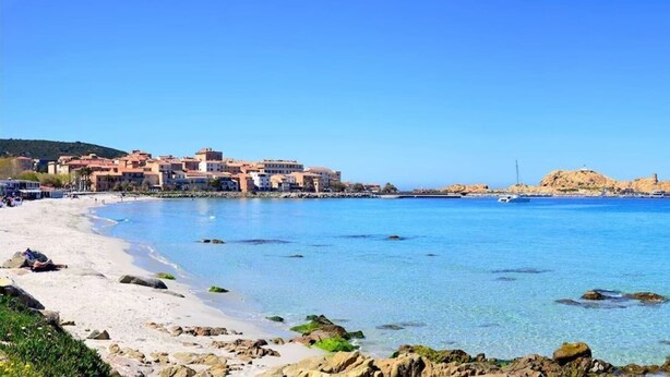 A coastal town with a sandy beach, clear blue waters, and buildings along the shore. - Le Marina (L'île-Rousse)