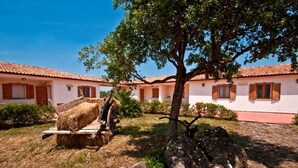 A traditional building with a tiled roof and wooden shutters, surrounded by a well-maintained garden with a large tree and hay bales.