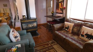 Ein gemütliches Wohnzimmer mit Kamin, einer Couch mit gemusterten Kissen, einem Couchtisch und einem Essbereich mit Tisch und Stühlen.