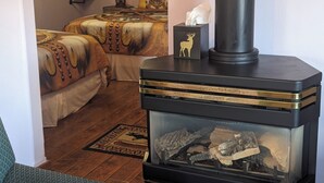 Ein gemütlicher Raum mit Kaminofen, einem Bett mit gemusterten Betttextilien, einem Nachttisch mit Laterne und einem an der Wand befestigten Regal mit Büchern.