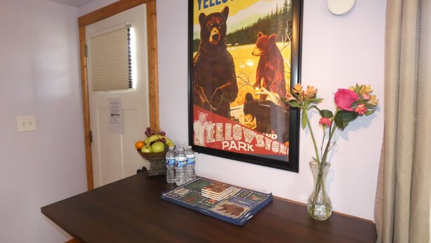 Ein Esstisch mit einem gerahmten Poster von Yellowstone, einer Obstschale, Wasserflaschen und einer Vase mit Blumen.