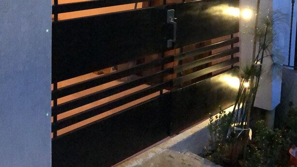 Una entrada moderna a un edificio con una reja metálica negra, una señal de calle y un pequeño jardín con plantas.